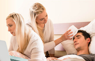 The photo shows a young woman working in front of a laptop. The same woman can be seen to the right in the photo, where she is wiping an ill man’s forehead.
