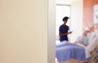 Bildet viser en sykepleier som står ved sengen til et døende menneske.