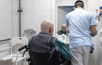 Bildet viser en mannlig sykepleier som steller en eldre pasient på badet