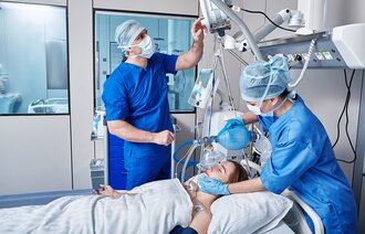 The photo shows two intensive care nurses standing by the bed of a patient being ventilated.