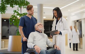 Bildet viser en pasient i rullestol med helsepersonell rundt seg