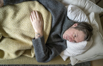 Illustrasjonsbilde av forkjølet mann på sofaen.