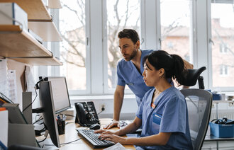 Bildet viser to sykepleiere som har overlevering av informasjon på vaktrommet