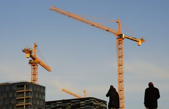 Bildet viser en byggeplass med to mennesker i siluett i forgrunnen