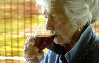 Bildet viser en eldre kvinne som drikker rødvin