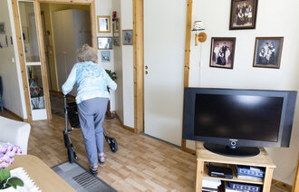 Bildet viser en eldre kvinne med rullator i sitt hjem