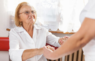 Bilde viser eldre dame som hjelpes av en pleier.