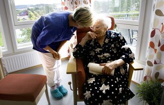 Bildet viser en eldre kvinne på velferdssenter. Får omsorg fra en av de ansatte.