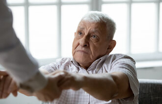 Bildet viser en eldre mann som holder hendene til noen utenfor bilderammen