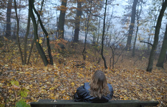 Bilde viser en dame som sitter på en benk med ryggen til