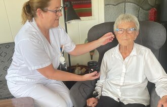 Bildet viser en pasient som får hjelp til å sette på plass høreapparatet