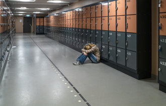 Bildet viser en ungdom som sitter i en korridor