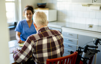 Bildet viser en mann som sitter med ryggen til kamera, vendt mot en pleier.