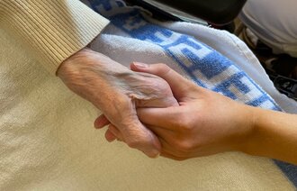 Bildet viser en sykepleier som holder hånden til en eldre pasient