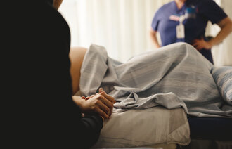 Bildet viser en kvinne som skal føde. I bakgrunnen: en jordmor.