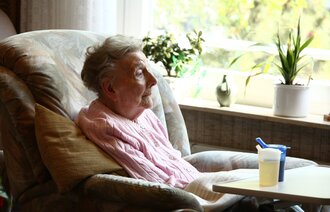 Bildet viser en eldre kvinne som sitter i en stol.
