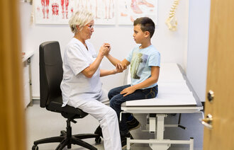 Bildet viser en eldre kvinnelige lege som undersøker en ung gutt.
