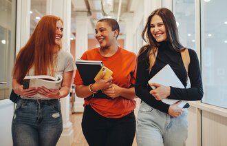 Bildet viser tre studenter som går i en gang på skolen og ler sammen