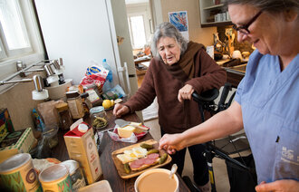 Bildet viser en hjemmesykepleier som tilbereder et måltid til brukeren.