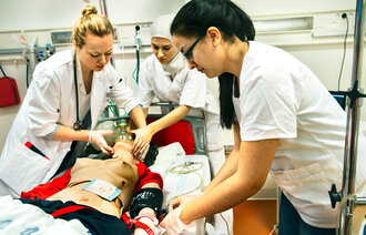 Sykepleier- og legestudenter øver på en akuttsituasjon med en dukke i sykesengen.