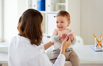 En blid baby sitter på et bord og blir undersøkt av en helsearbeider.