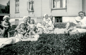 Historisk, gammelt bilde av sykepleiere med små barn på gresset utenfor Bergen kommunale mødrehjem.