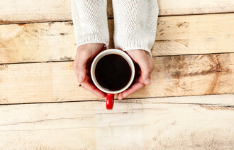 Kvinne med kaffe En kvinnes hender holder en kopp med kaffe på et rustikt trebord
