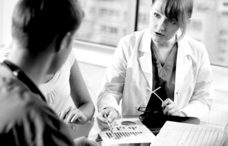 Bildet viser ei dame i hvit frakk som viser to personer et ark med et diagram på.