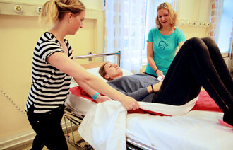 Bildet viser bedriftsfysioterapeutene Anne Aschehoug Loftu og Sigrunn Haug Simensen viser hvordan man ved hjelp av forflytningsteknikk kan flytte «pasient» Gina Grøtting Sjöström oppover i sykesengen på en mindre belastende måte.