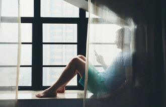 Ung mann sitter med mobil bak gardin.