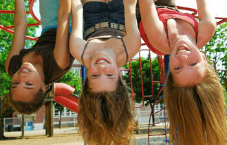 Tre barn som "henger" opp ned i et klatrestativ