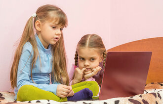 Bildet viser to jenter som sitter i en seng og ser på en bærbar pc.