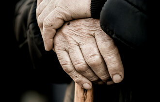 Nærbilde av eldre hender på en stokk