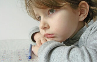 Bildet viser en tankefull jente som øver på å skrive bokstaver på et papir.