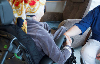 En gamel dame som sitter i en stol og holder en pleier i hånden.