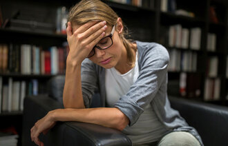 Bildet viser en kvinne som sitter i en stol og hviler pannen i hånden.