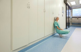 Bildet viser en pleier som sitter på huk lent mot en vegg og ser sliten ut.