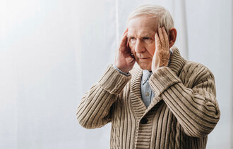 Bildet viser en eldre mann som holder hendene mot tinningene.