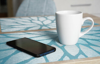 Mobiltelefon og kaffekopp på bord.