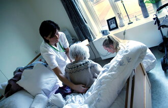 Bildet viser to sykepleiere som hjelper en pasient i sengen hennes på Karmøy sykehjem.