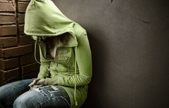 Ung jente, sittende med hettegenser og bøyd rygg