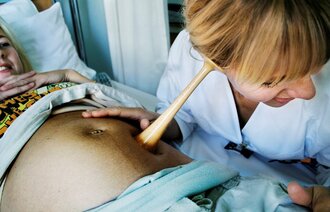 Bildet viser en jordmor som lytter på en mage med jordmorstetoskop.