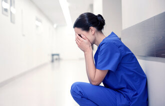 Umotivert og lei sykepleier holder hendene foran ansiktet.