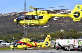 Bildet viser et ambulansehelikopter som er i ferd med å lette, og et som står på bakken i bakgrunnen