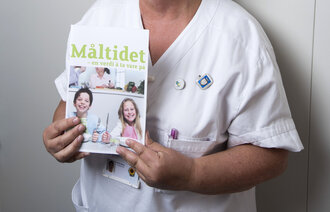 Torill Berg poserer med bladet "Måltidet", under høydemålingsstativ ved overvektsklinikken.