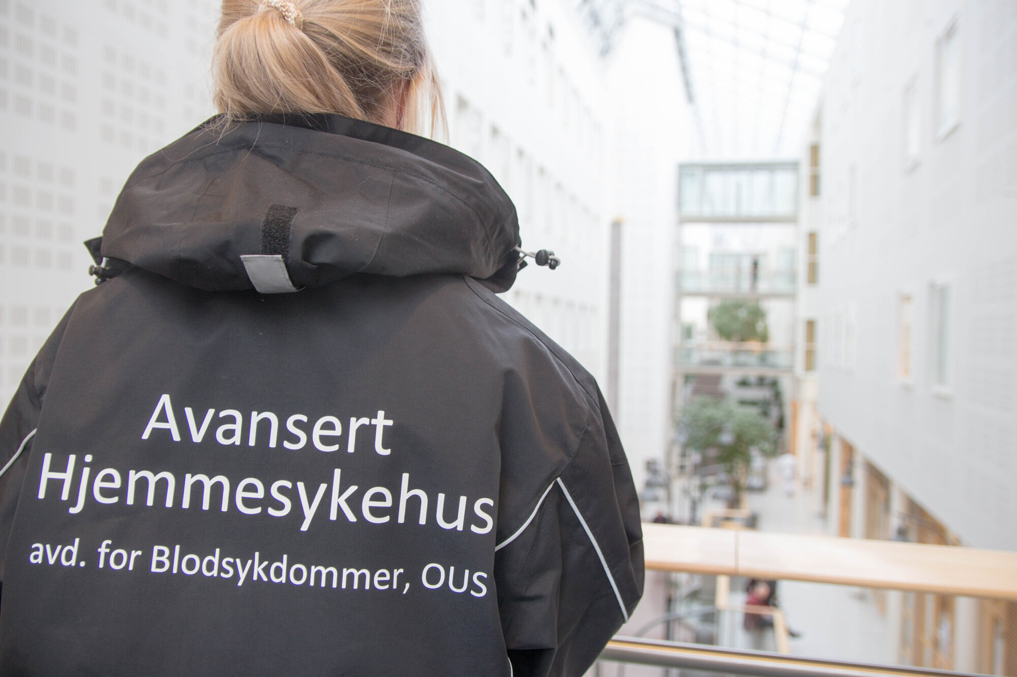 Bildet viser en sykepleier bakfra med jakke det står avansert hjemmesykehus på.