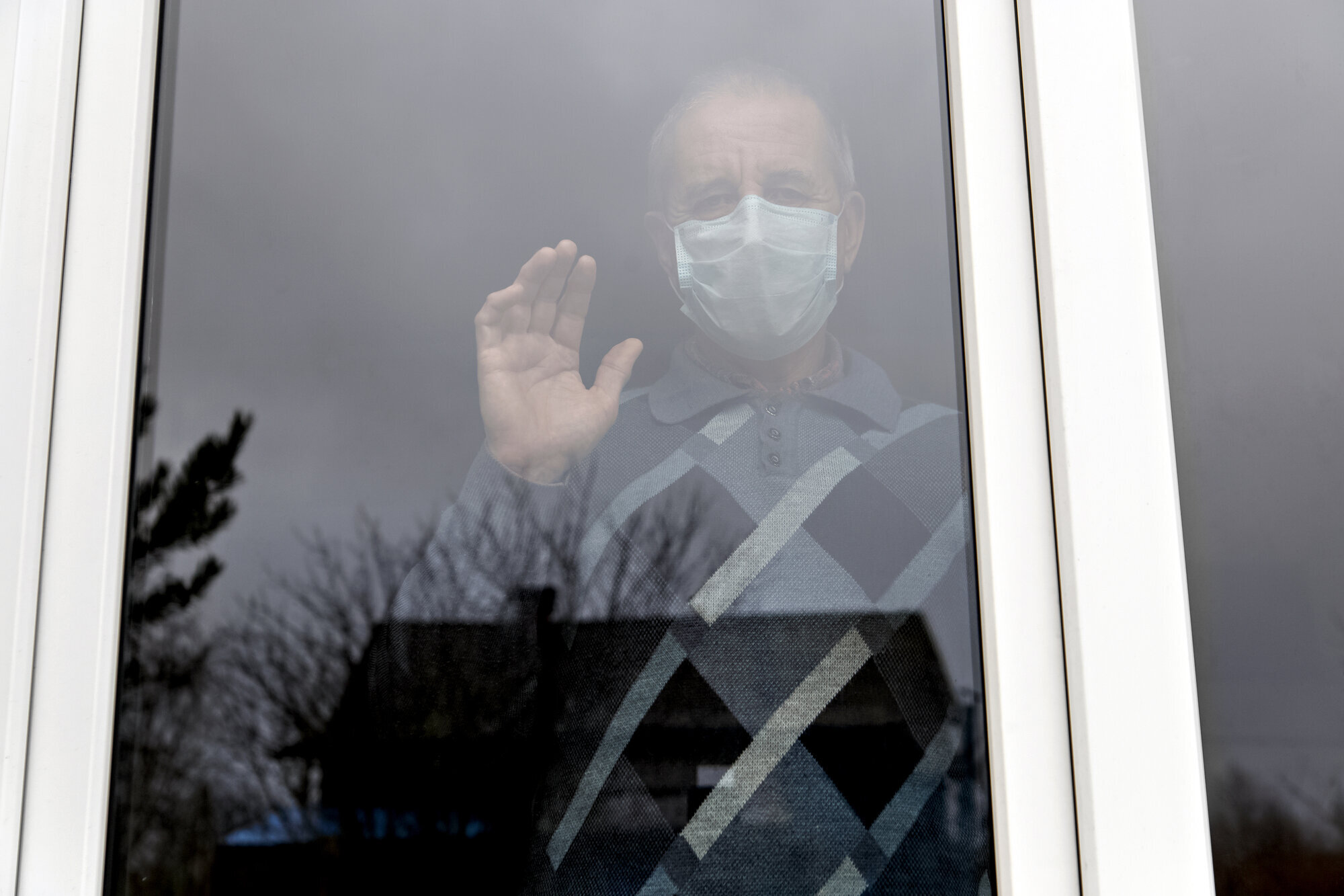 Eldre mann med munnbind bak vindu