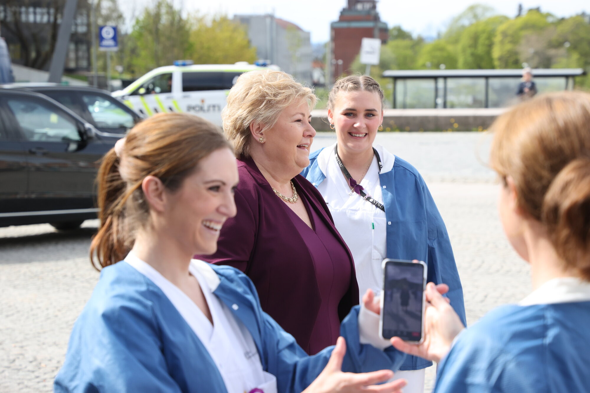 Bildet viser Ida Gerø med mobiltelefon, i bakgrunnen statsminister Erna Solberg og andre sykepleiere.