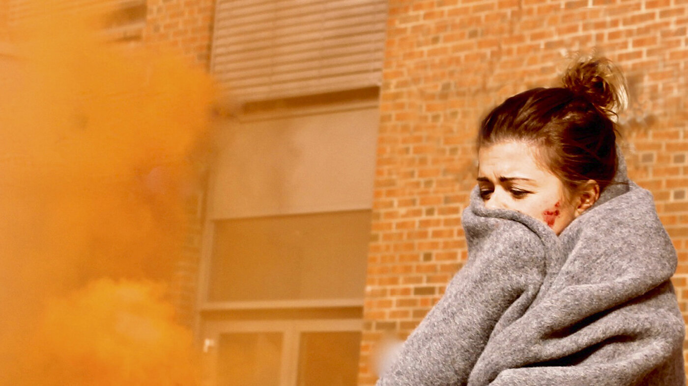 Bildet viser en skadet kvinne med et pledd rundt seg. Det er røykskyer rundt henne.