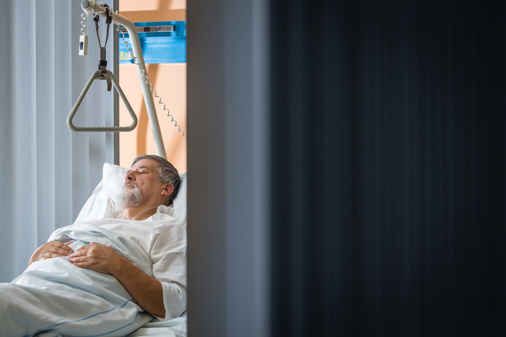 Bildet viser en eldre mann som ligger i en seng og ser ut av vinduet